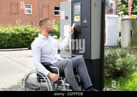 Homme handicapé en fauteuil roulant payant un ticket de parking utilisant la machine Banque D'Images