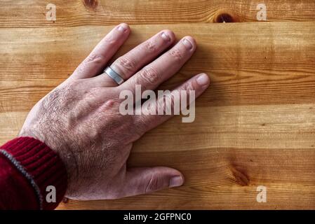 Vue de dessus de la main d'un homme portant un anneau argenté sur une table en bois Banque D'Images