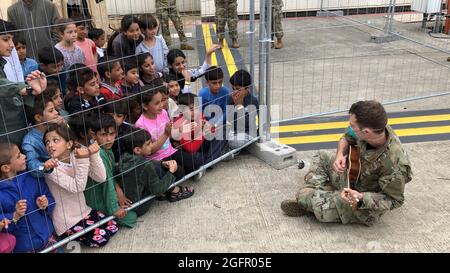 Ramstein Miesenbach, Allemagne. 24 août 2021. Un aviateur de la US Air Force joue le ukulele pour les enfants afghans afin des divertir à la base aérienne de Ramstein le 24 août 2021 à Ramstein-Miesenbach, en Allemagne. La base aérienne de Ramstein fournit un hébergement temporaire aux personnes évacuées d'Afghanistan dans le cadre de l'opération alliés refuge. Credit: Planetpix/Alamy Live News Banque D'Images