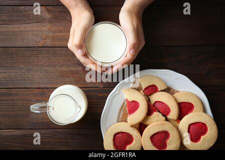Mains féminines avec lait et biscuits sur table en bois, vue de dessus