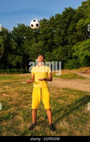 L'homme s'entraîne et améliore le contrôle du ballon de football sur les berges de sable herbacé Banque D'Images