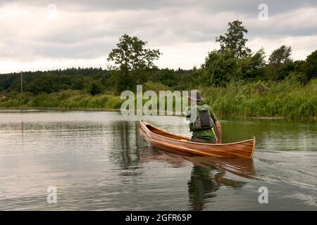 L'homme pagaie un canoë en bois Canadian Cedar Strip en descendant une rivière calme dans le Norfolk England UK Banque D'Images