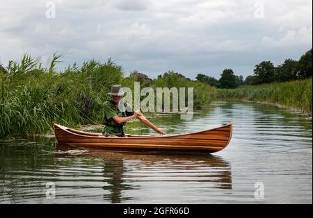 L'homme pagaie un canoë en bois Canadian Cedar Strip en descendant une rivière calme dans le Norfolk England UK Banque D'Images