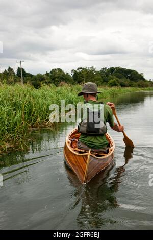 L'homme pagaie un canoë en bois Canadian Cedar Strip en descendant une rivière calme dans le Norfolk England UK Banque D'Images