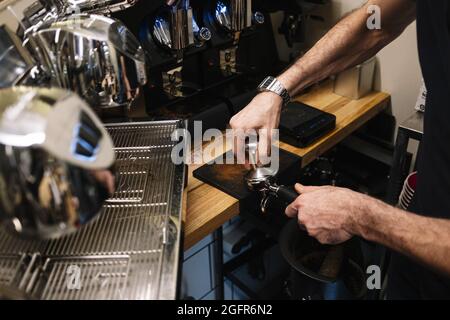 Gros plan des mains du barman en pressant un café moulu dans le porte-filtre Banque D'Images