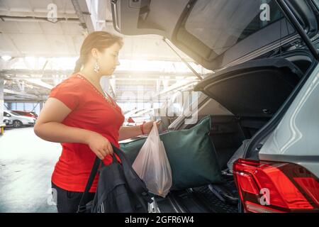 Les jeunes filles après avoir fait du shopping chargent des sacs dans le coffre de voiture dans le parking du centre commercial. Banque D'Images