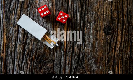 Deux dés rouges avec allumettes à l'intérieur d'une boîte d'allumettes blanche sur une table rustique en bois Banque D'Images