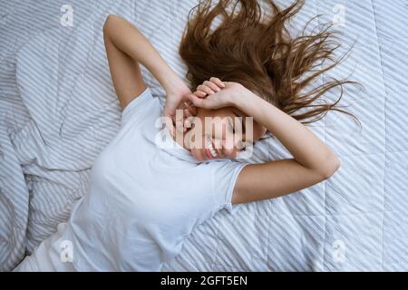 Une jeune femme se réveille après une bonne nuit de sommeil dans son lit. Sensation d'excitation : une femme heureuse en pyjama s'étire au lit après s'être réveillée le matin. Commencez une nouvelle journée avec un concept de sourire Banque D'Images