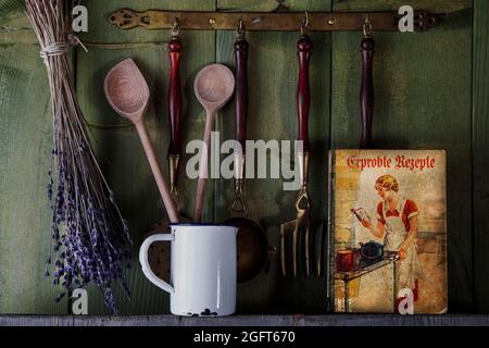 ancien livre de cuisine avec ustensiles de cuisine devant un mur en bois vert Banque D'Images