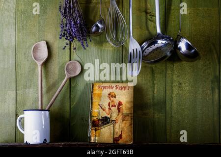 ancien livre de cuisine avec ustensiles de cuisine devant un mur en bois vert Banque D'Images