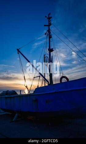 Bateau de pêche bleu rouille sur la mer au coucher du soleil. Les rayons de soleil jaunes sont réfléchis à la surface de l'eau. Le concept de pêche, transport, trave Banque D'Images