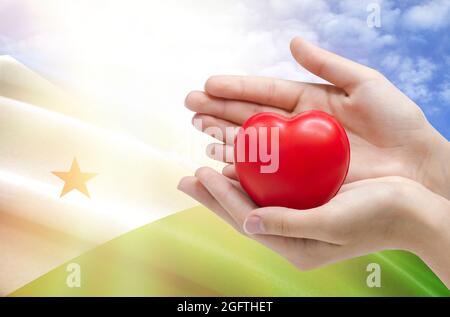 Les mains de l'enfant tiennent un coeur sur le fond du drapeau de Djibouti, concept de soins de santé. Banque D'Images