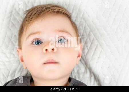 Portrait en gros plan d'un bébé de neuf mois. Bleu yeux rouge chevreau allongé sur le lit regardant l'appareil photo Banque D'Images