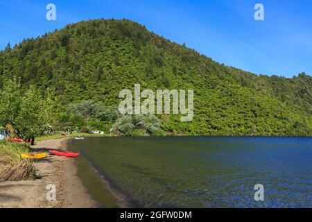 Lac Okareka dans le district des lacs de Rotorua, Nouvelle-Zélande. Les kayaks reposent sur le rivage au camping du ministère de la conservation Banque D'Images