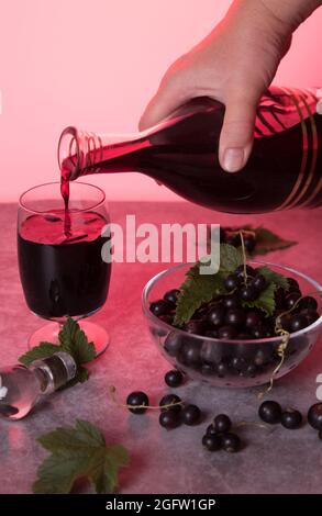 La main d'une femme verse de la liqueur de cassis maison dans un verre d'un carafe. Banque D'Images