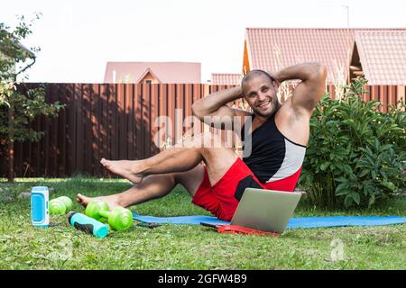 Le jeune homme entre pour le sport à la maison dans l'arrière-cour en été, l'entraînement en ligne. L'athlète fait la presse sur le tapis dans le jardin Banque D'Images