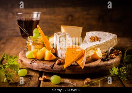 Plateau de fromages, assortiment de différents fromages avec verre de vin rouge, raisins sur table en bois Banque D'Images