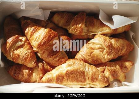 Délicieux croissants sur parchemin dans un panier lors d'un pique-nique ensoleillé à l'extérieur. Vue de dessus sur les croissants fraîchement cuits au soleil. Du pain savoureux et des en-cas Banque D'Images