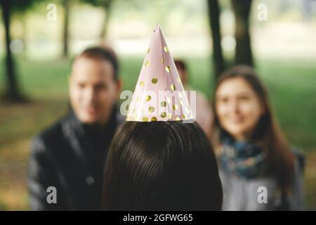 Élégant chapeau de fête rose gros plan sur la tête de femme, vue arrière. Jeune femme heureuse élégante en casquette de fête célébrant son anniversaire avec sa famille et ses amis au picni Banque D'Images