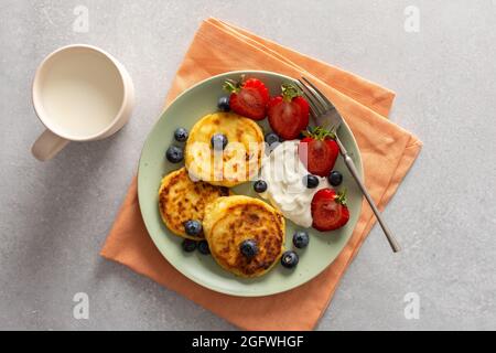 Crêpes au fromage cottage avec fraises, bleuets et crème sure, tasse avec lait, délicieux petit déjeuner, vue sur le dessus Banque D'Images