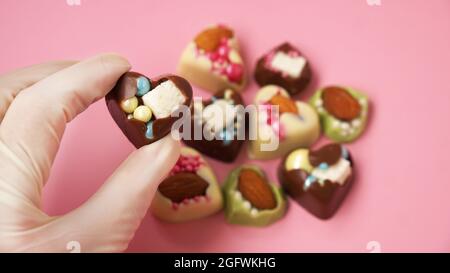 La main en gants du chef pâtissier tient un bonbon en forme de cœur. Bonbons sur fond rose. Friandises de la Saint-Valentin Banque D'Images