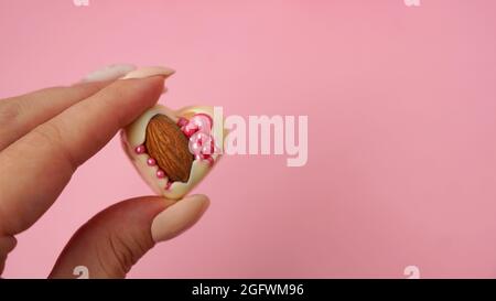 La main contient des bonbons au chocolat blanc aux amandes. Bonbons en forme de cœur. Bonbons faits main sur fond rose Banque D'Images
