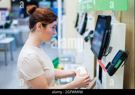 Une femme frustrée utilise un comptoir de caisse libre-service. La fille ne comprend pas comment acheter indépendamment des provisions dans le supermarché sans un vendeur Banque D'Images