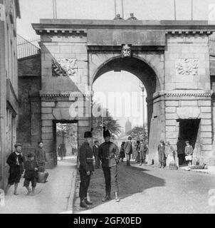 Vue du début du XXe siècle sur la porte des évêques, dans les murs de la ville de Derry, alias la ville de Londonderry, en Irlande du Nord. La porte originale a été remplacée en 1789 par une arche triomphale pour marquer le premier centenaire de la fermeture des portes par les apprentis garçons de Derry. L'architecte était H.A. Baker, avec les têtes sculptées représentant la rivière Foyle (externe) et la rivière Boyne (interne) conçue par Edward Smyth, qui avait sculpté les treize têtes fluviales sur la maison personnalisée de Dublin en 1784. Banque D'Images