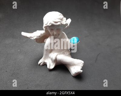 Deko Figur weiß Engel Kind sitzend mit einer blauen Kugel in der Hand Banque D'Images