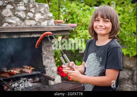 Les enfants grillent de la viande. Joyeux adolescent qui fait le barbecue sur le grill sur la nature. Camping familial et barbecue Banque D'Images