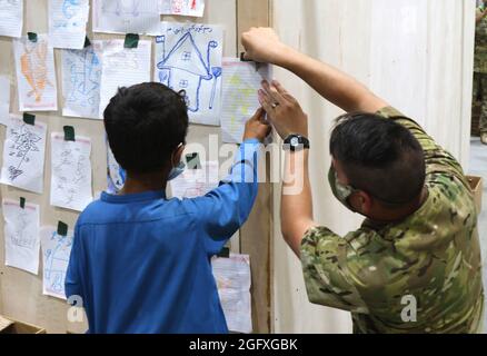 Un soldat central de l'armée américaine aide un garçon afghan évacué à exposer son travail d'art avec d'autres au Camp Buehring, au Koweït, le 25 août 2021. Les soldats se sont joints aux activités et ont passé du temps avec les enfants pendant que leurs familles ont passé les processus d'arrivée à l'installation. (É.-U. Photo de l'armée par PFC. Katelynn Bissell) Banque D'Images