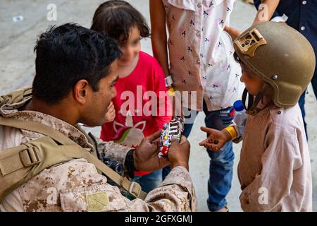 Une marine américaine avec un corps de mission maritime à but spécial - intervention en cas de crise - Commandement central, donne des bonbons aux enfants lors d'une évacuation à l'aéroport international Hamid Karzaï, Kaboul, Afghanistan, août 24. Les membres du service américain aident le ministère d'État à effectuer une opération d'évacuation non combattantes (NEO) en Afghanistan. (É.-U. Photo du corps marin par lance Cpl. Nicholas Guevara) Banque D'Images