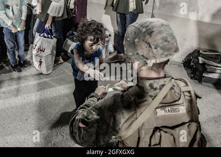 Une marine américaine avec la 24e unité expéditionnaire maritime (MEU) donne à un enfant une lumière chimique à jouer avec lors d'une évacuation à l'aéroport international Hamid Karzaï, Kaboul, Afghanistan, août 25. Les membres du service américain aident le ministère d'État à effectuer une opération d'évacuation (NEO) non combattue en Afghanistan. (É.-U. Photo du corps marin par le sergent d'état-major. Victor Mancilla) Banque D'Images