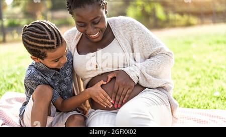 Bonne famille africaine s'attendant à un autre bébé - Afro mère et son fils touchant le ventre enceinte faisant la forme du coeur avec les mains Banque D'Images