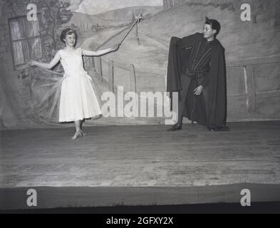 1956, historique, une jeune fille et un garçon agissant dans la pantomine, Jack et le Beanstalk, sur une scène dans leurs costumes, Angleterre, Royaume-Uni. La fille dans une robe de fête et tenant une baguette joue le caractère de la femme de fée et le garçon dans une tenue et cape est le personnage principal de Jack. Célèbre fée ou conte folklorique anglais, Jack et la Beanstalk est une ancienne fable sur un garçon pauvre qui, dit par sa mère de vendre la vache de sa famille sur un marché, l'échange plutôt pour cinq haricots 'magique', qui se développent en une manomanette enornous qui se développe dans les nuages, Que Jack monte et a des aventures. Banque D'Images