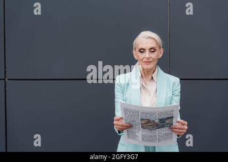 Femme d'affaires senior lisant le journal près d'un bâtiment à l'extérieur Banque D'Images