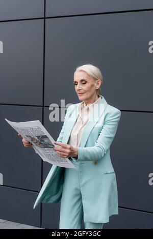Femme d'affaires âgée lisant des nouvelles près d'un bâtiment à l'extérieur Banque D'Images