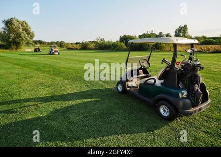 Une voiture de golf avec des clubs de golf et de l'équipement se trouve sur un terrain de golf en herbe avec une ombre longue pendant le golf Banque D'Images