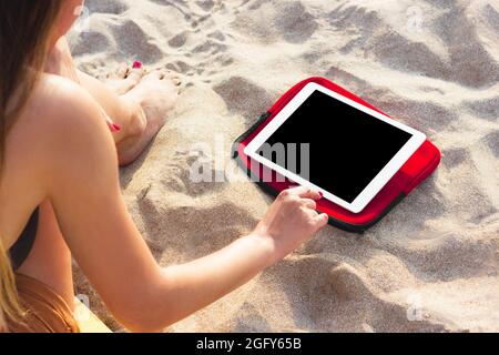 Jeune femme sportive utilisant une tablette sur la plage pour regarder des cours de fitness. Communication sans fil et Internet pour un style de vie actif, le yoga et l'exercice Banque D'Images