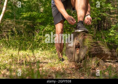 Le sportif enfile les lacets de ses jambes dans des baskets gros plan l'athlète court dans le parc à l'extérieur, autour de la forêt, les arbres de chêne vert herbe youn Banque D'Images