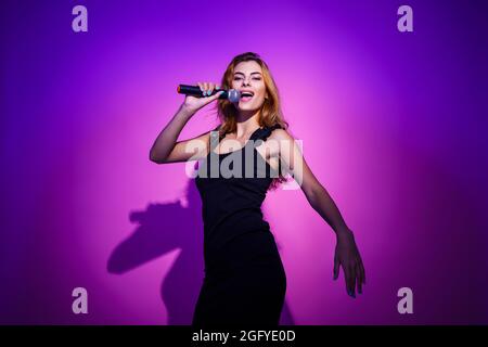 Photo portrait d'une femme tenant le microphone dans les mains isolées sur fond rose pastel Banque D'Images