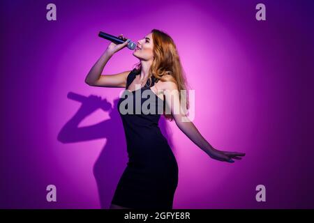 Photo portrait d'une femme tenant le microphone dans les mains isolées sur fond rose pastel Banque D'Images