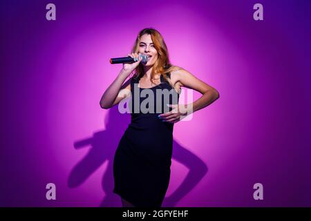 Photo portrait d'une femme tenant le microphone dans les mains isolées sur fond rose pastel Banque D'Images