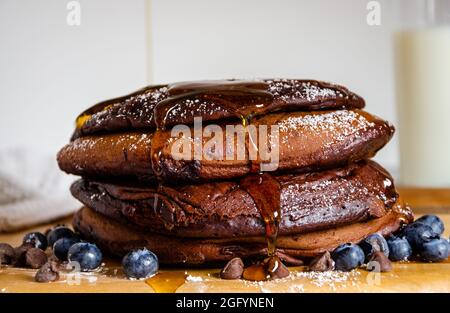 Pile de crêpes au chocolat avec sirop d'érable en poudre saupoudrés et bleuets au lait et copeaux de chocolat Banque D'Images