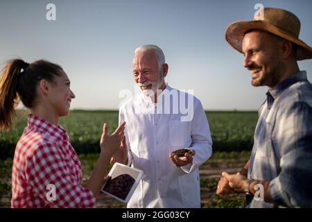 Jeune femme tenant une tablette souriante discutant de la qualité de la terre. Jeune agriculteur souriant, regardant de côté. Biologiste expert tenant la boîte de Pétri avec le sol s Banque D'Images