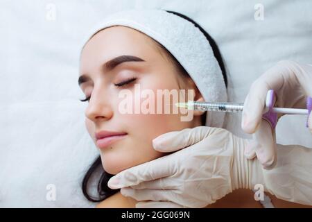 Sourit et augmente la lèvre.Esthéticienne médecin mains faisant la procédure de beauté au visage de la femme avec la seringue.La bouche de la jeune femme contournant avec Banque D'Images