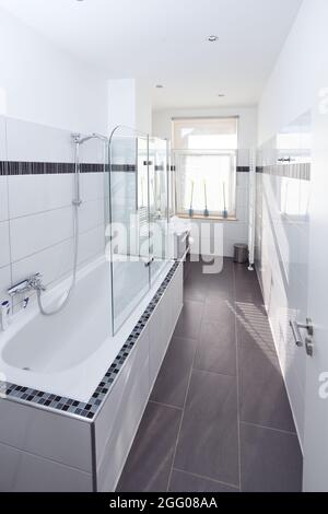 élégante salle de bains élégante maison hôtel carrelage blanc sol gris baignoire douche fenêtre de rétroéclairage Banque D'Images
