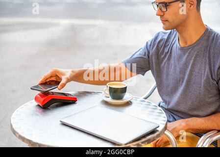 Youn latin homme payant avec le téléphone mobile dans la machine Banque D'Images