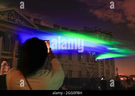 Greenwich, Londres, Royaume-Uni. 27 août 2021. Un visiteur prend des photos du spectacle. Lors de sa soirée de lancement publique officielle, « Borealis » de Dan Archer illumine le ciel au-dessus du Old Royal Naval College dans le Royal Borough de Greenwich. 'Borealis' est une reconstitution hypnotique des aurores boréales dans le ciel. Il fait partie du festival annuel de Greenwich et des Docklands, qui se tiendra du 27 août au 11 septembre 2021. Credit: Imagetraceur/Alamy Live News Banque D'Images