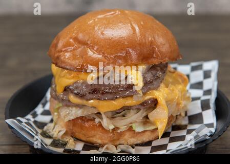 Grand double cheeseburger empilé haut avec les ingrédients et le fromage fondant sur les côtés pour un repas appétissant. Banque D'Images